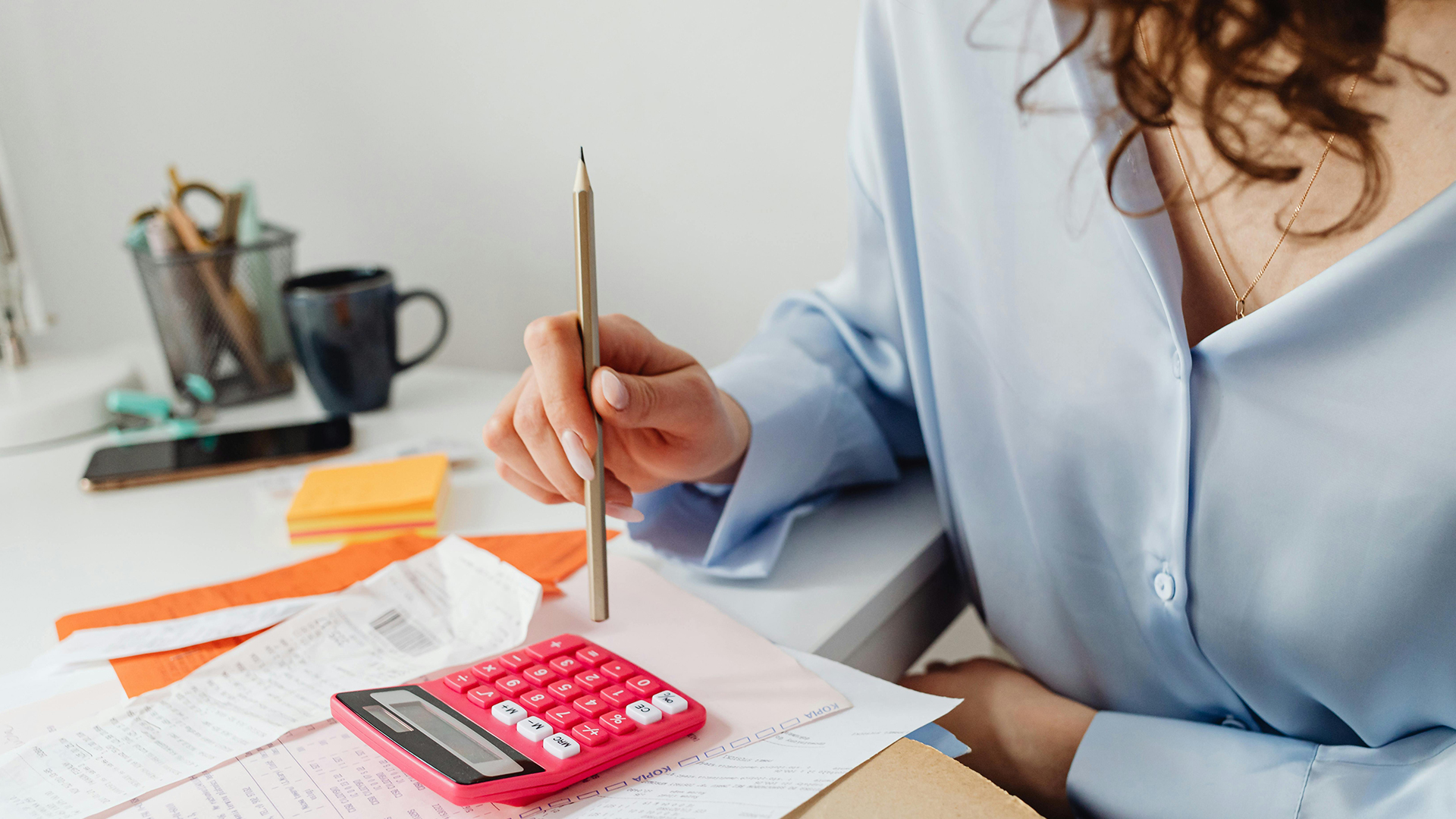 Person using calculator on desk next to receipts and invoices.