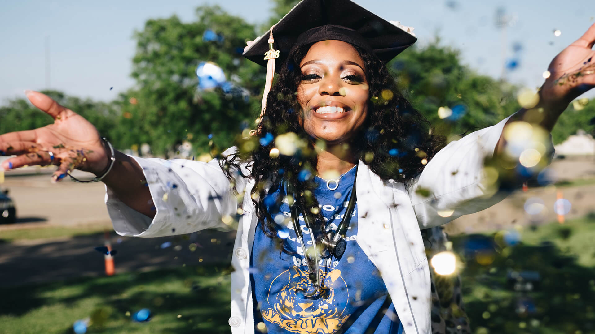 Young woman in a graduation gown and cap, smiling and throwing confetti.