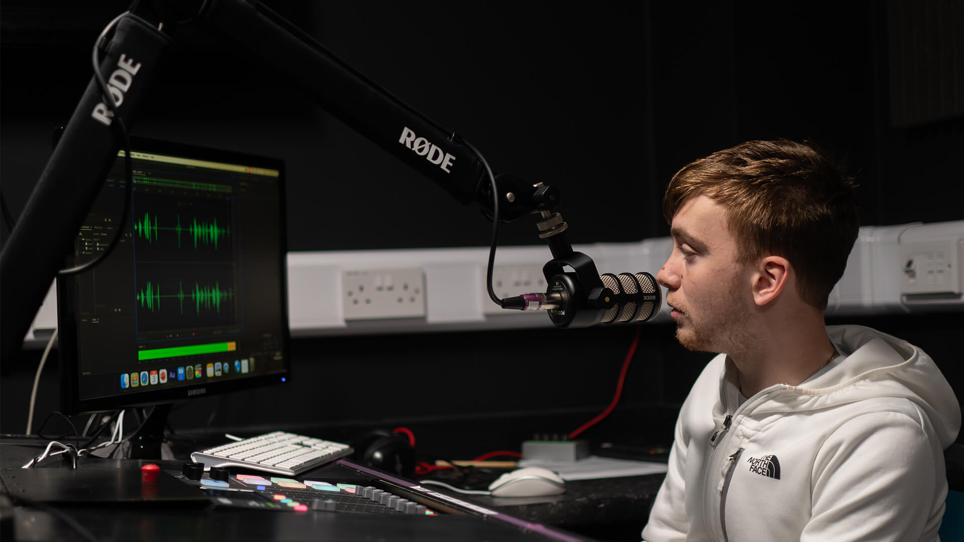 Young man sat in recording room with microphone.
