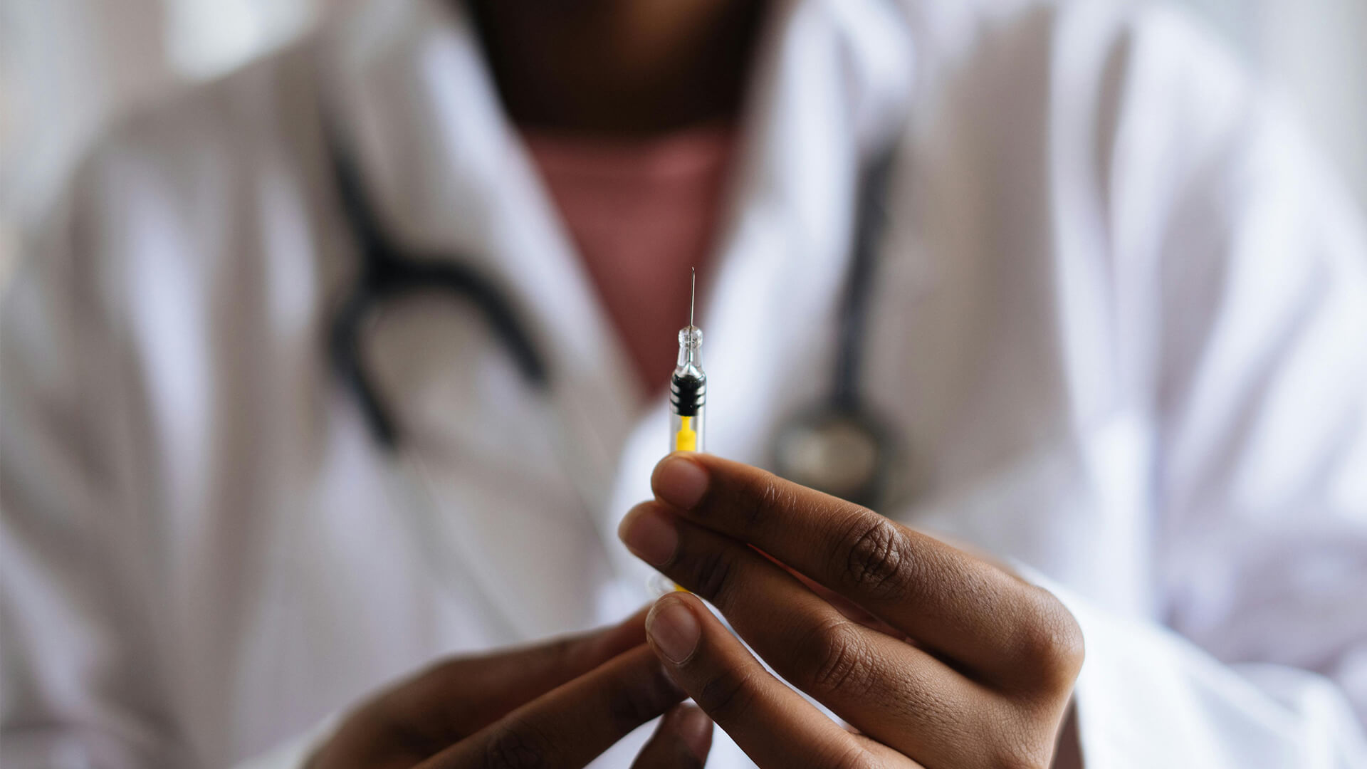Close up of person wearing doctors white jacket holding syringe.