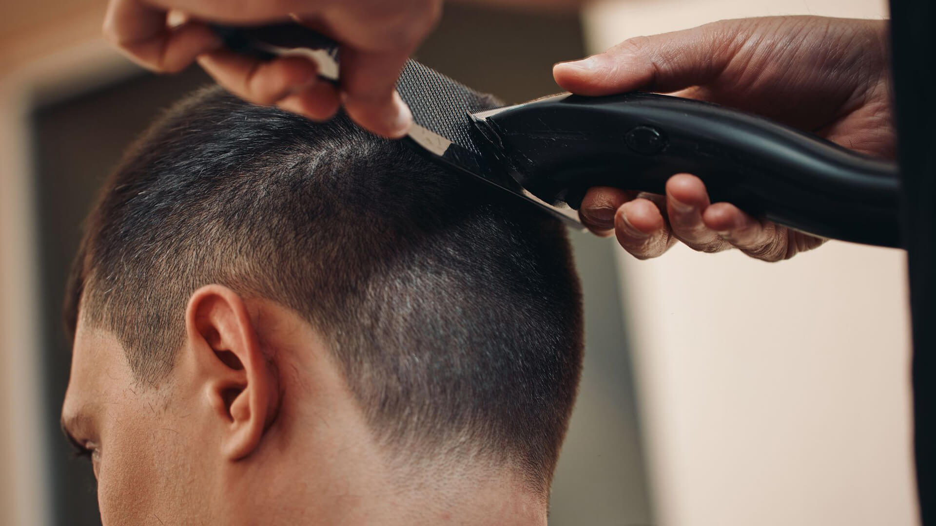 Young woman cutting a mans hair, and another barber cutting another mans hair in the background.