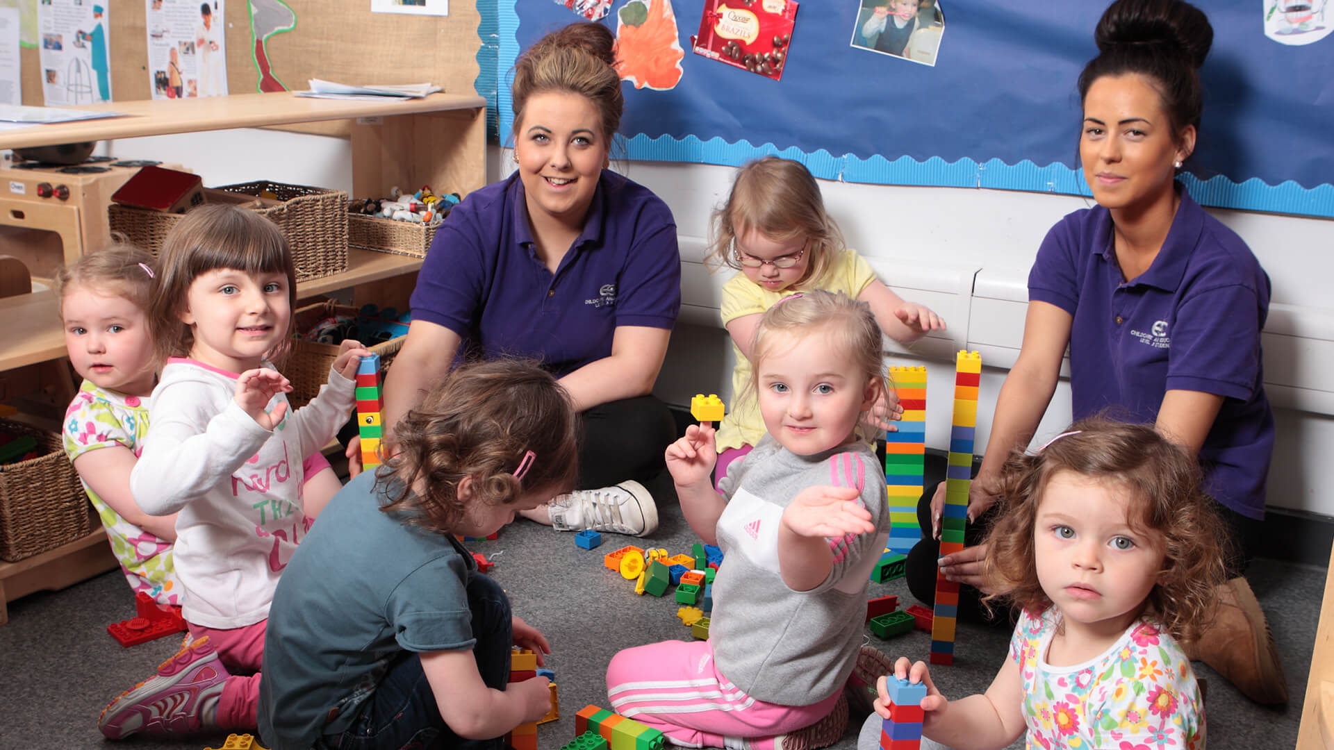 Two nursery nurses sitting with six small children playing with toys.