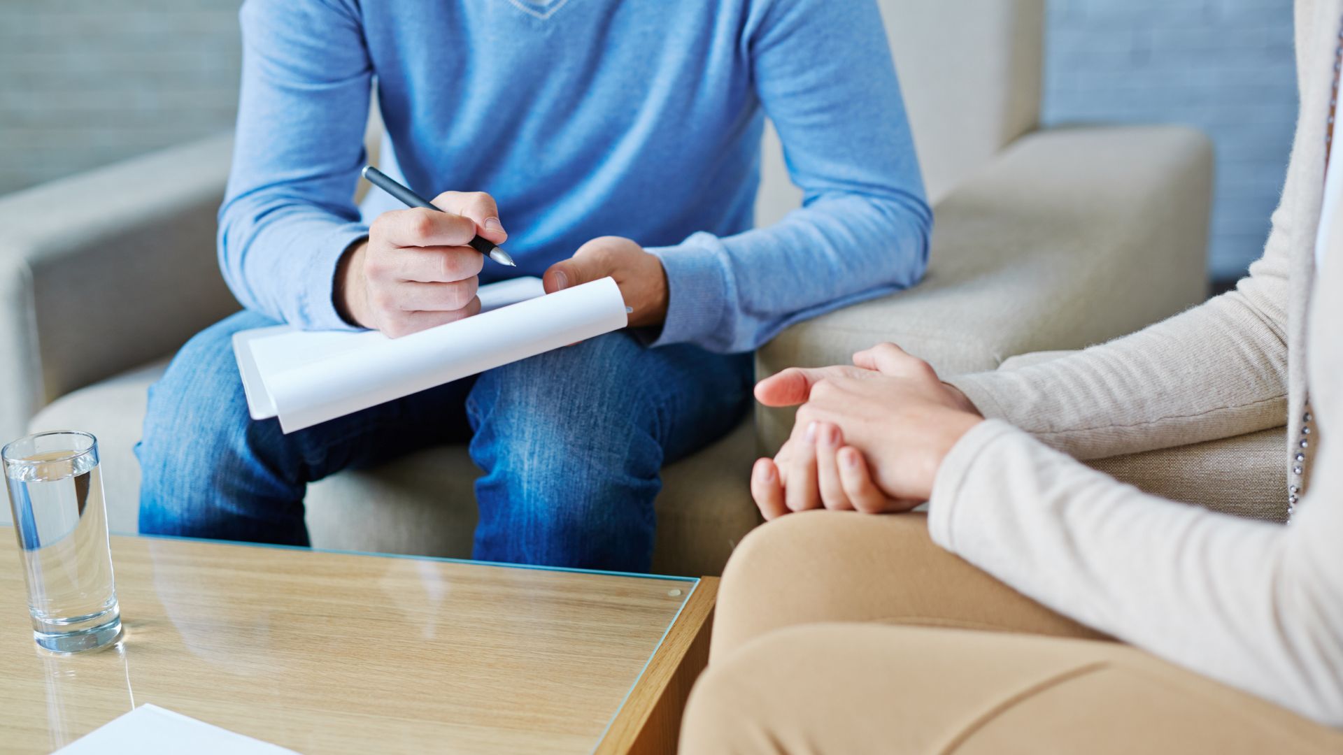 Person holding a clipboard and pen talking to another person with clapsed hands