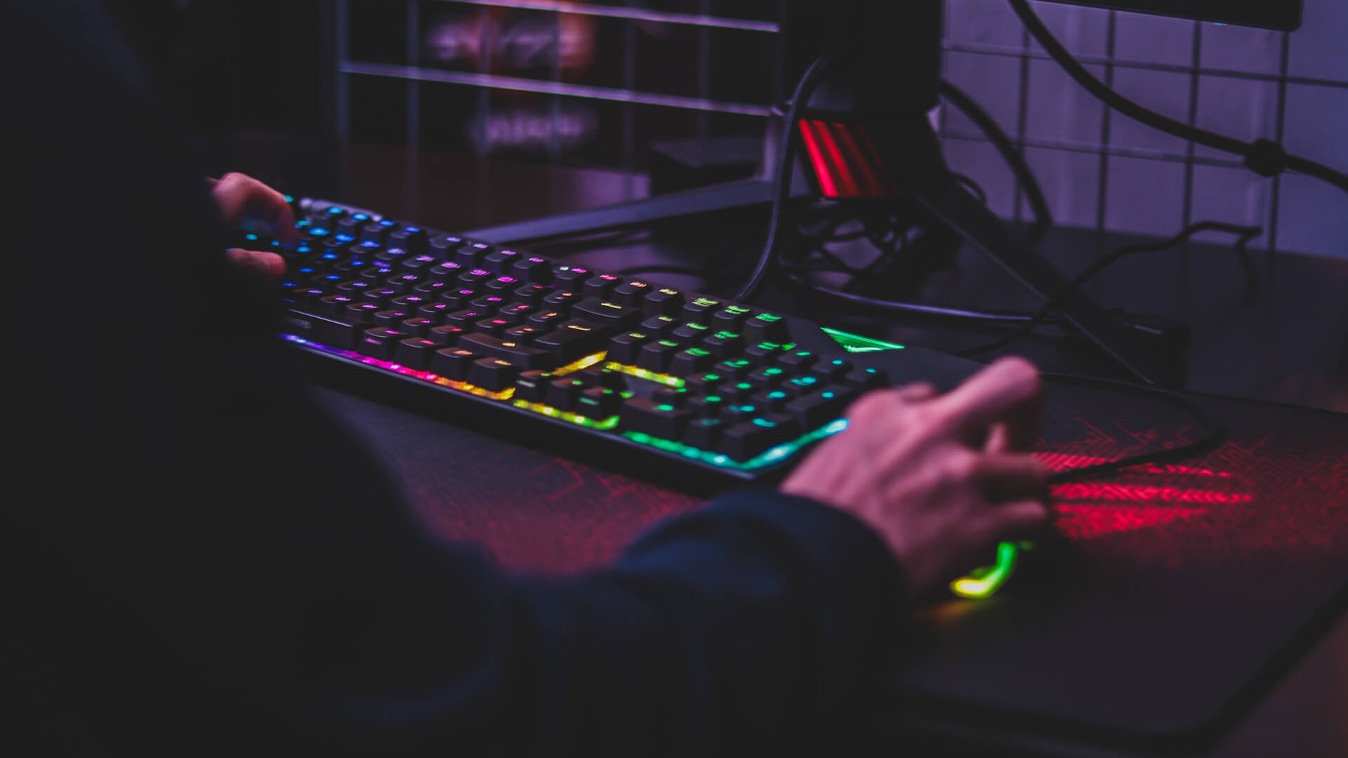 A keyboard with multi-colour lights on it and someone typing.