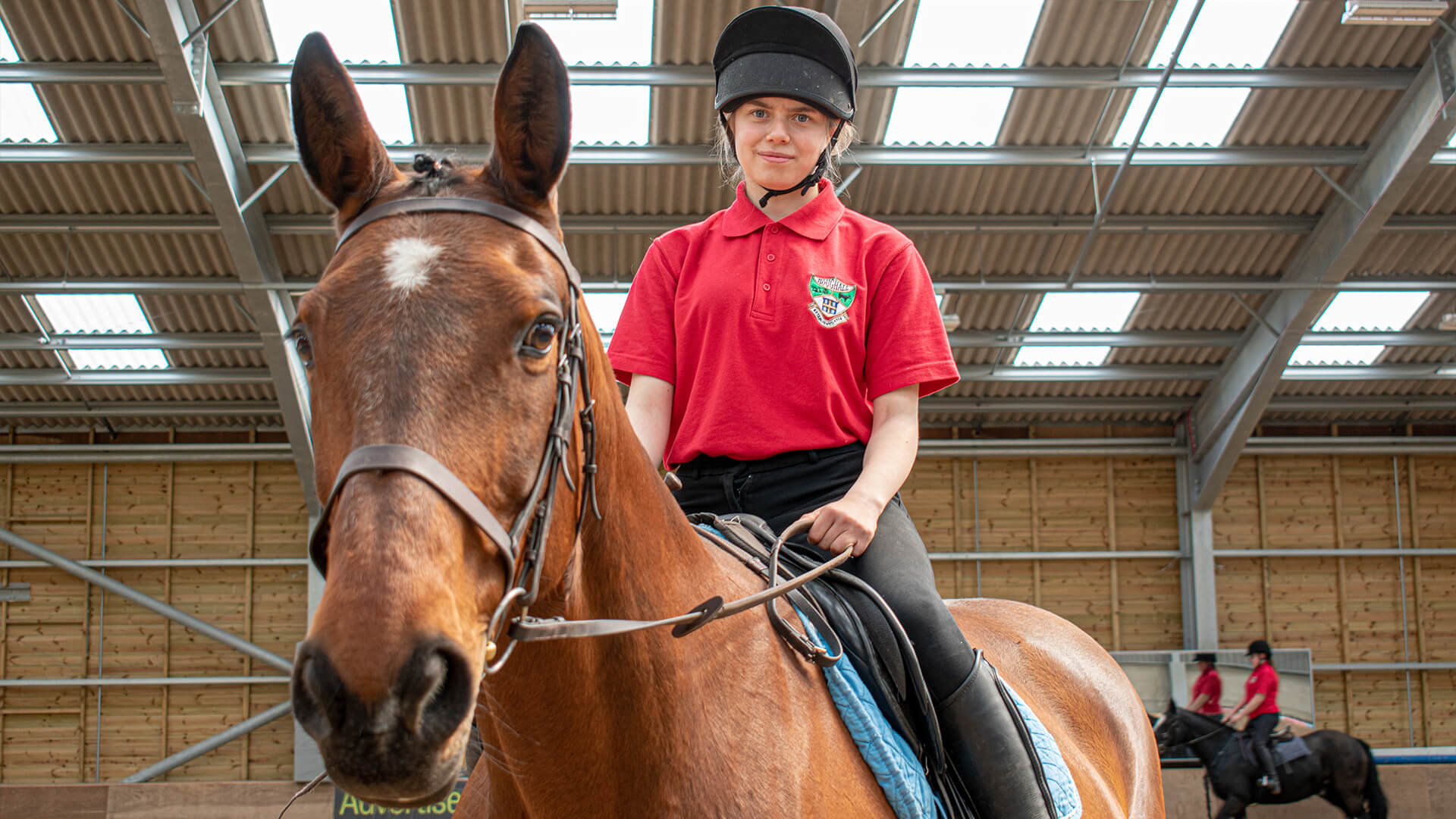 Young woman wearing riding gear whilst sat on a brown horse.