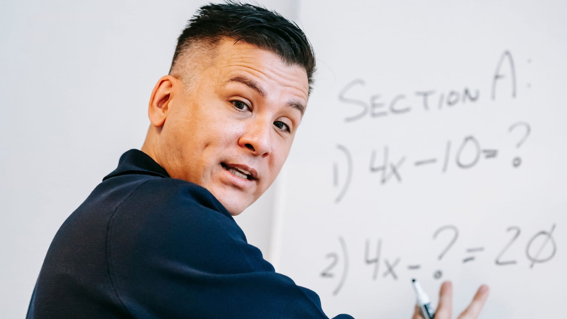 Teacher pointing at whiteboard with equations on