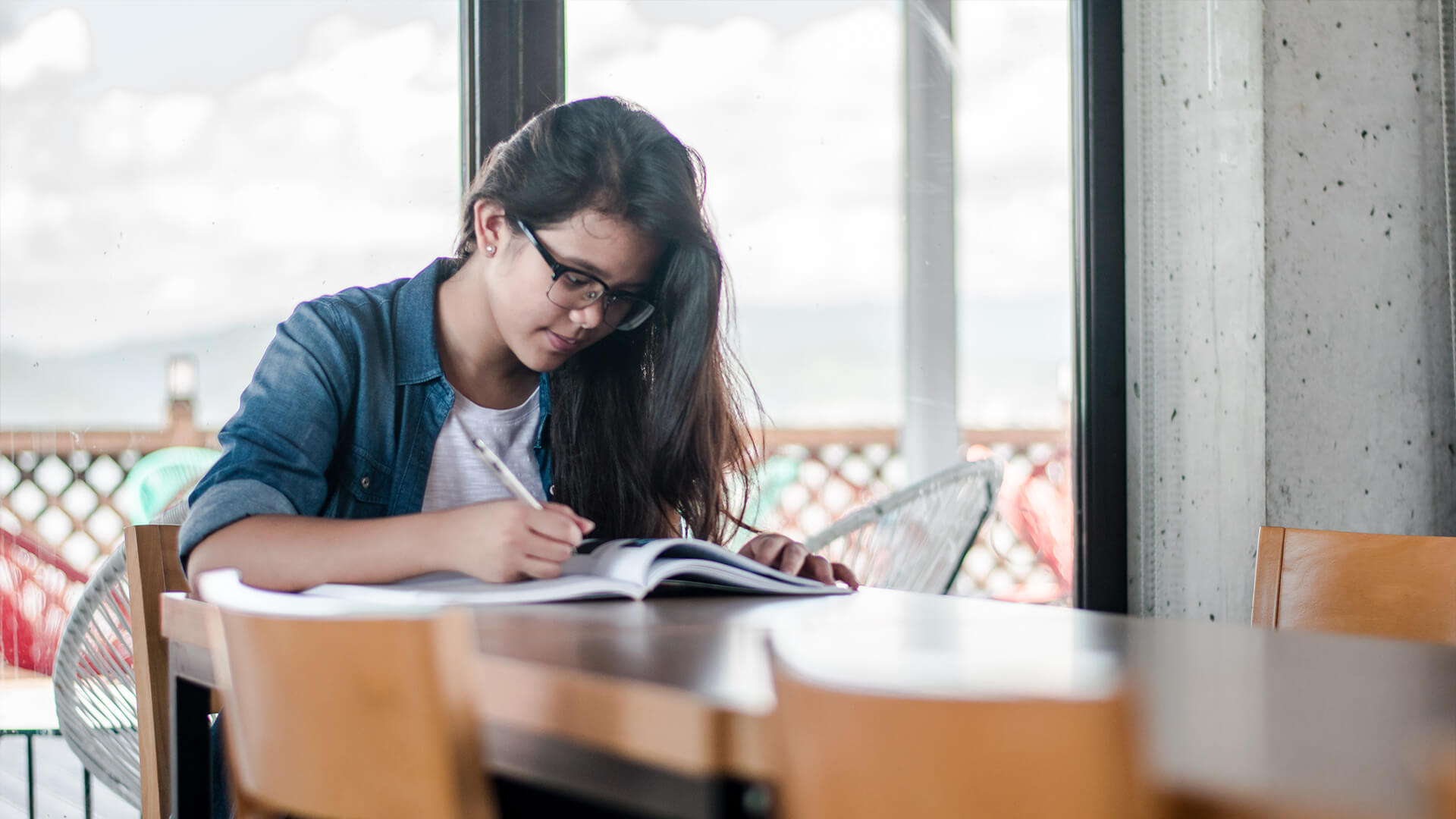 A young woman at a desk with a pen in her hand, working on a textbook.