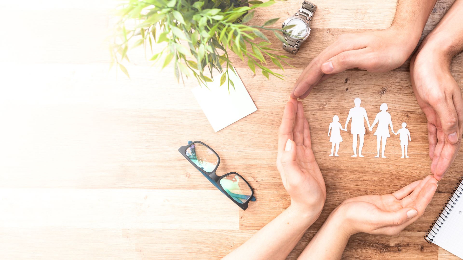 Hands surrounding cutouts of a family with two children and male and female parents holding hands