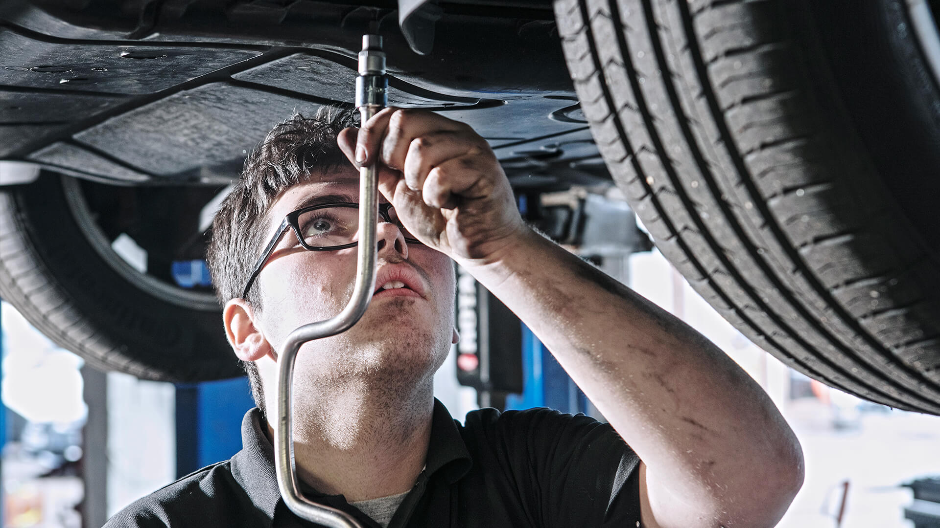 A young man in a high-vis jacket working on the underneath of a car.