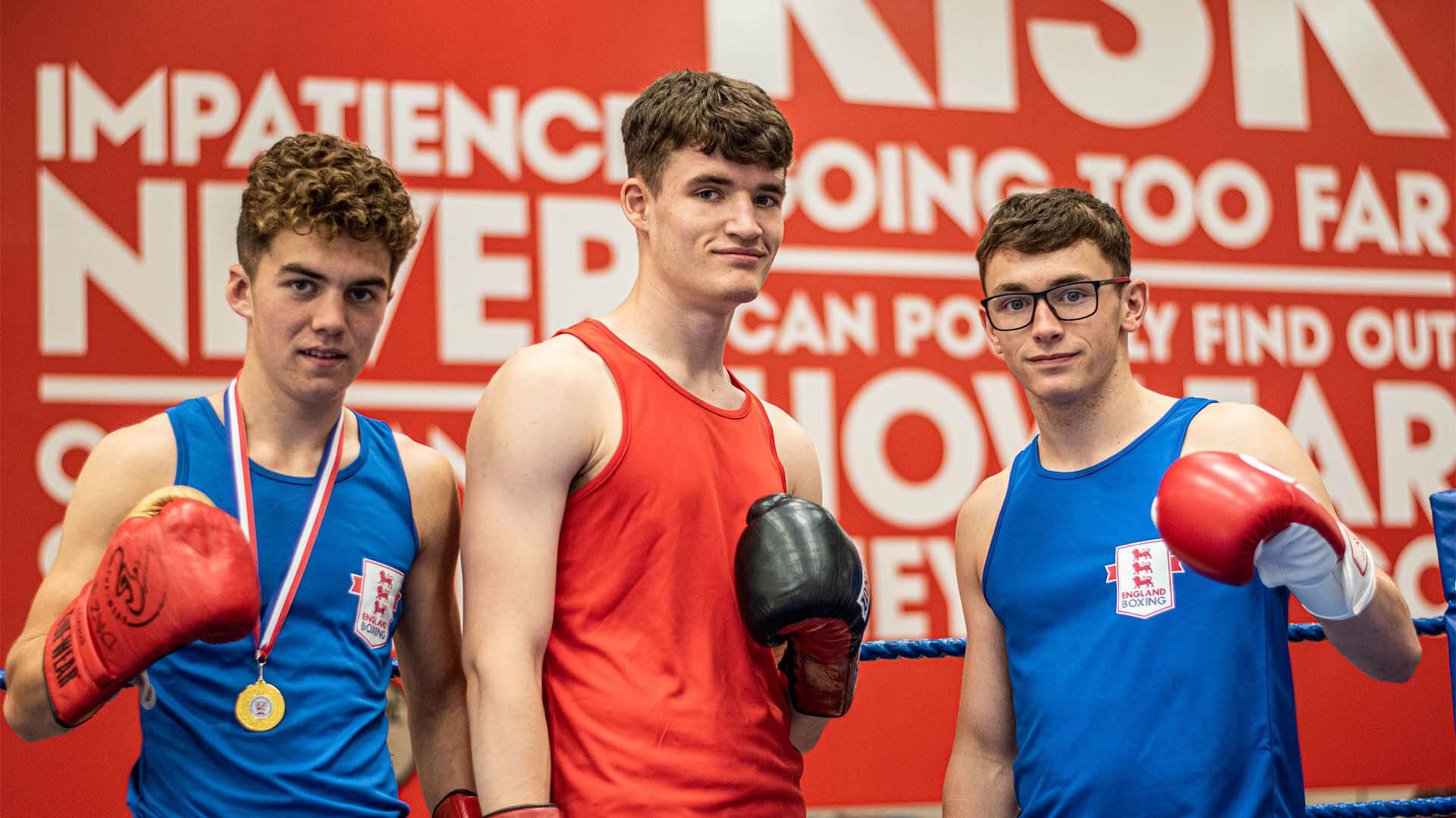 Three young men wearing boxing gear including boxing gloves in a boxing ring.