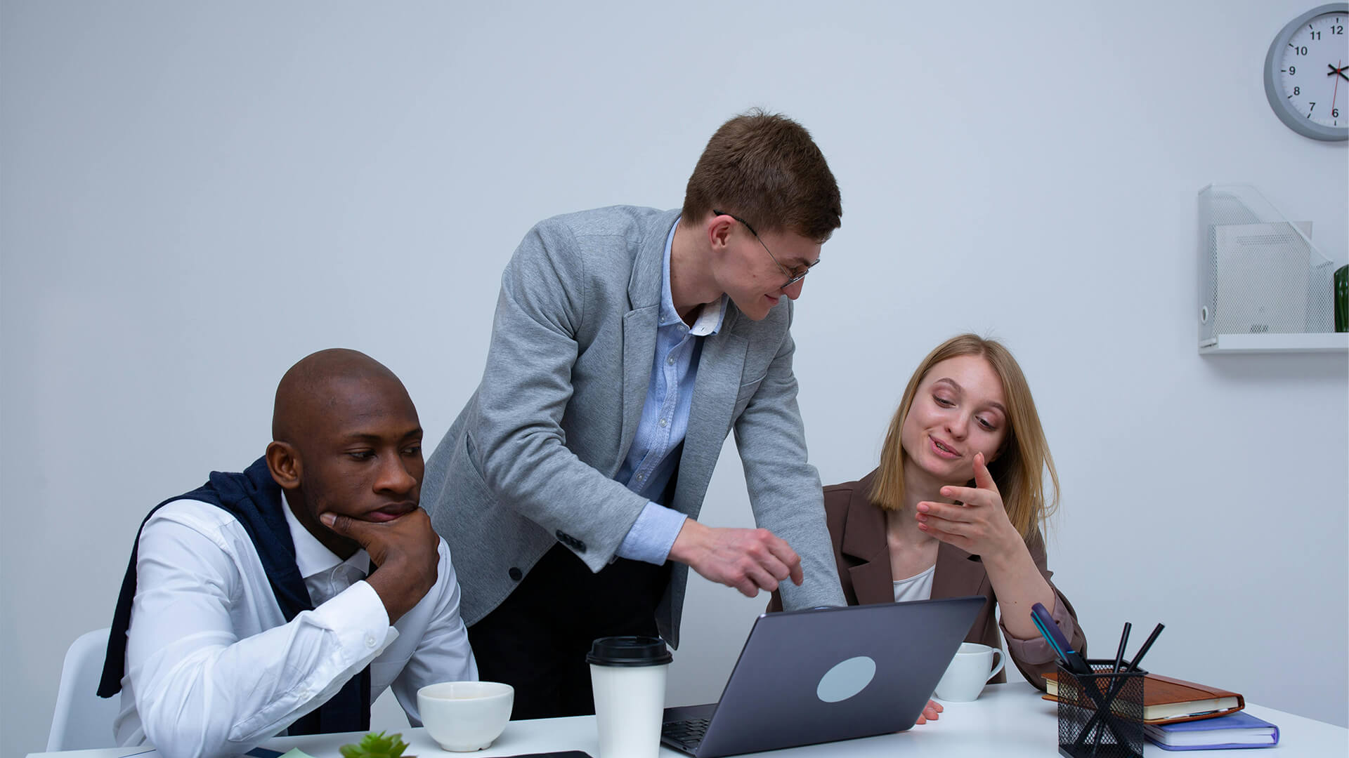 Man and two colleagues looking at laptops in office