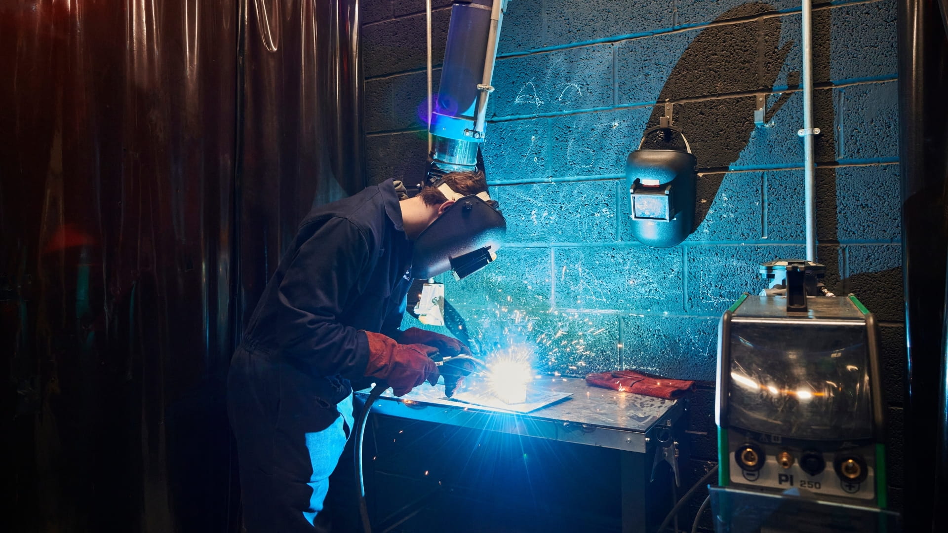 Person wearing mask welding with blue sparks flying
