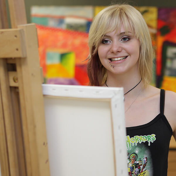 Young woman looking at an easel and smiling.
