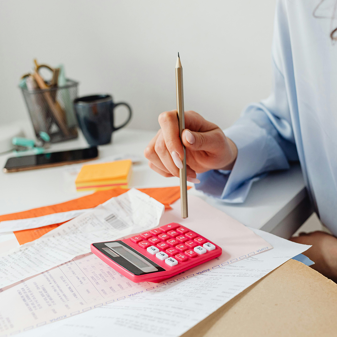 Person using calculator on desk next to receipts and invoices.