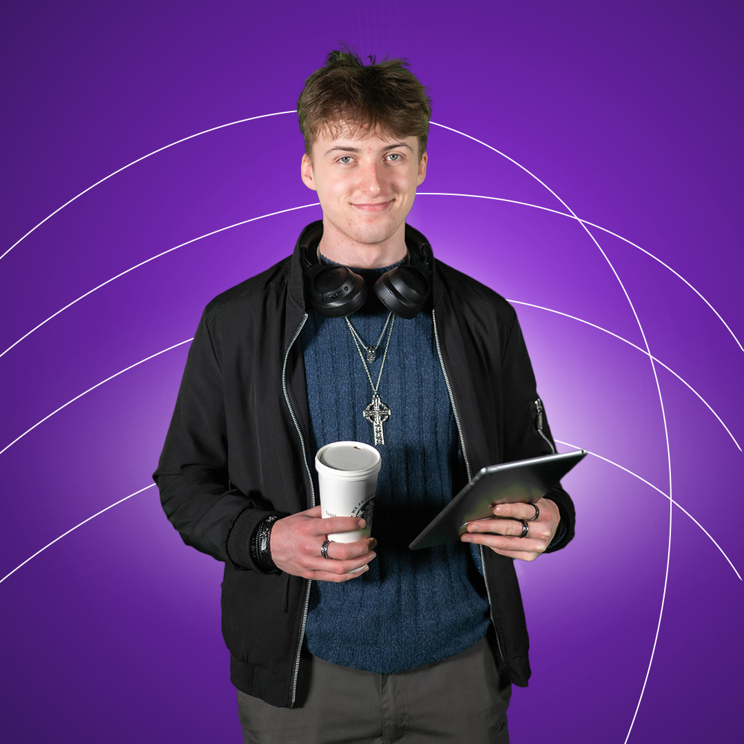 Young man holding starbucks cup in one hand and ipad in the other similing at camera on a purple background.
