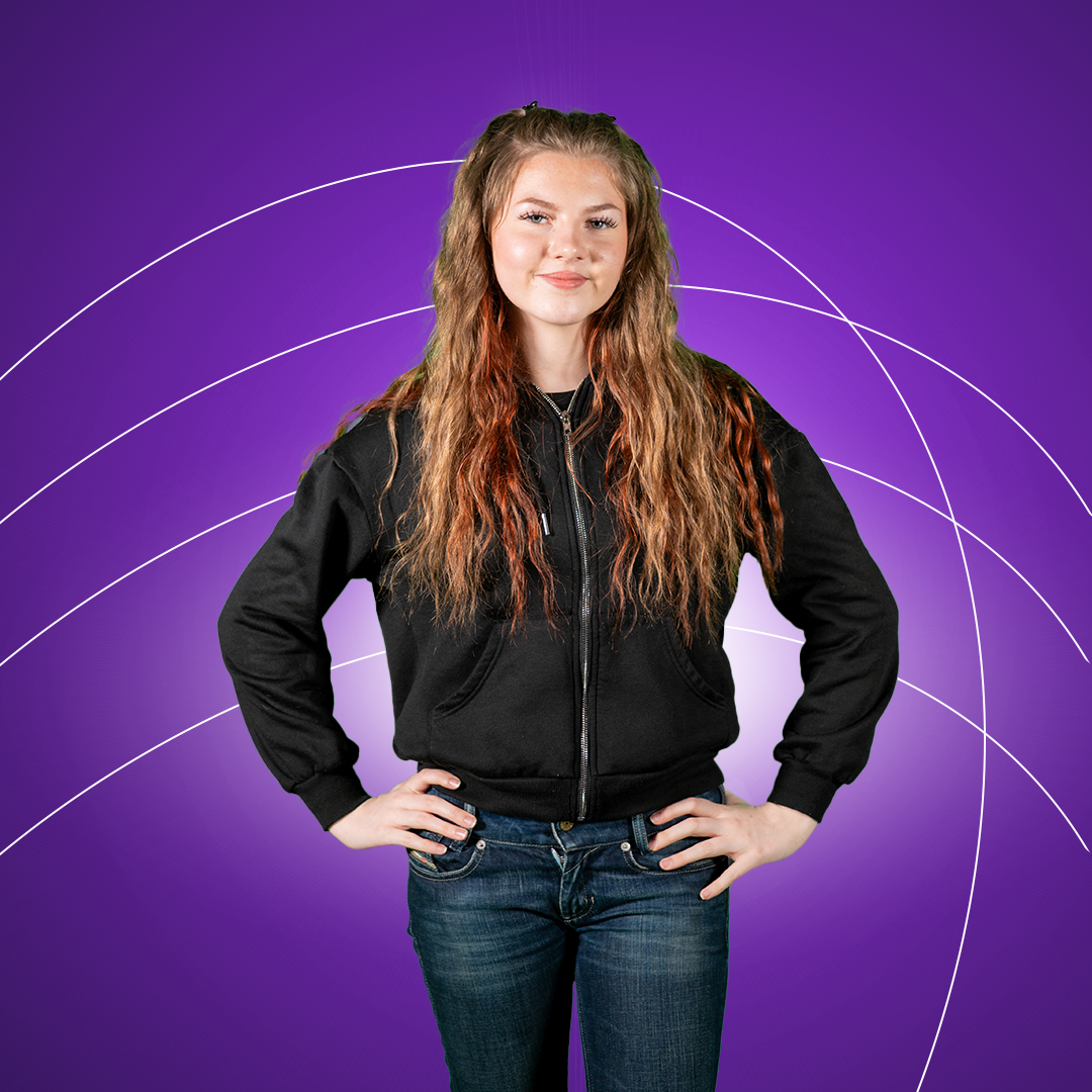 Young women standing with hands on hips smiling at camera on a purple background.