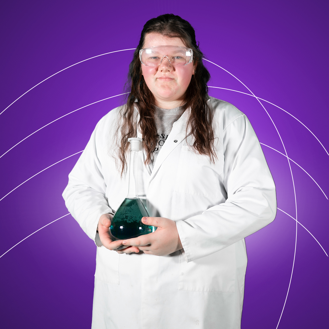 Young women holding conical flask wearing lab coat and safety glasses smiling at camera on a purple background.