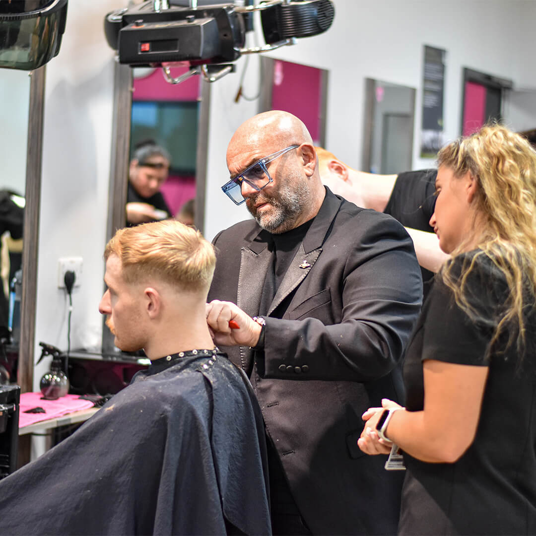 A man demonstrating to a young student how to barber whilst using a model.