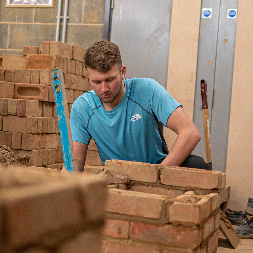 Student holding spirit level next to stack of bricks.