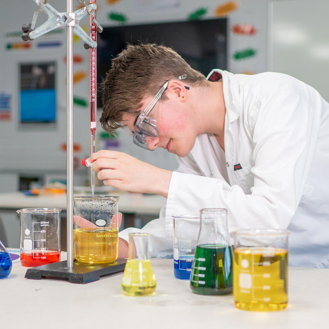 Young woman wearing a white lab coat and safety goggles, holding a beaker and doing a science experiment involving fire and sparks.