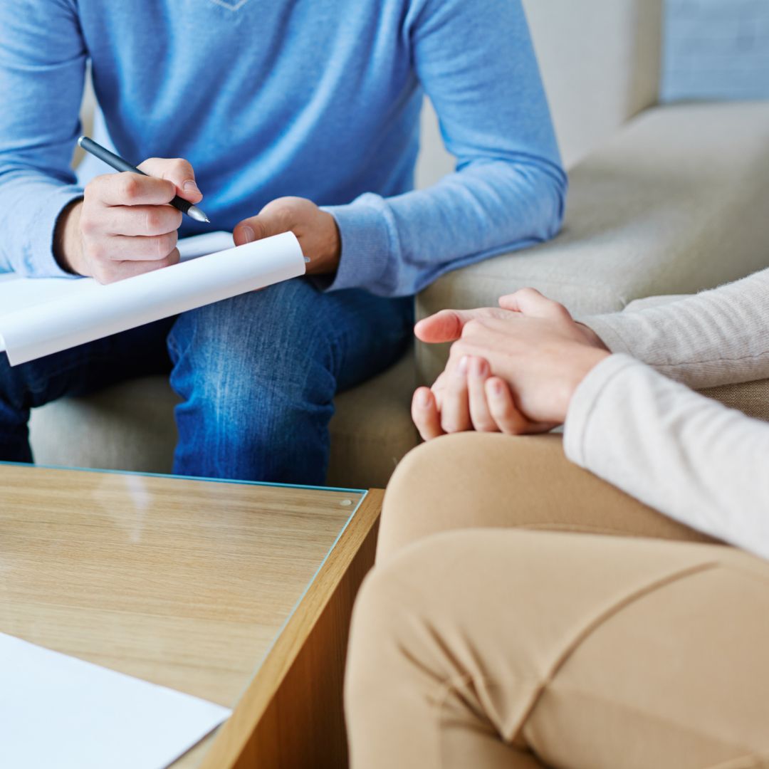 Person holding a clipboard and pen talking to another person with clapsed hands