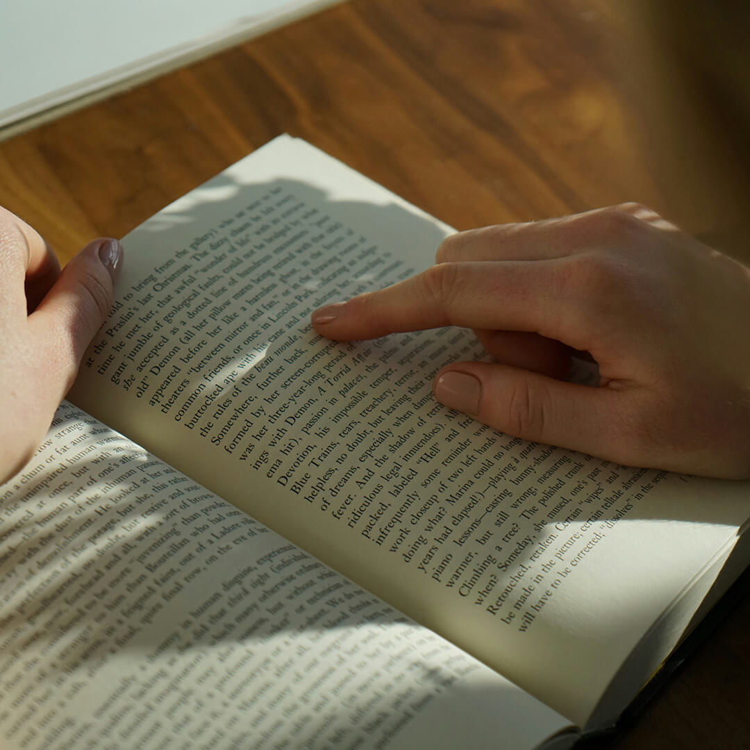 Young woman sat down and smiling at the camera whilst holding a textbook.