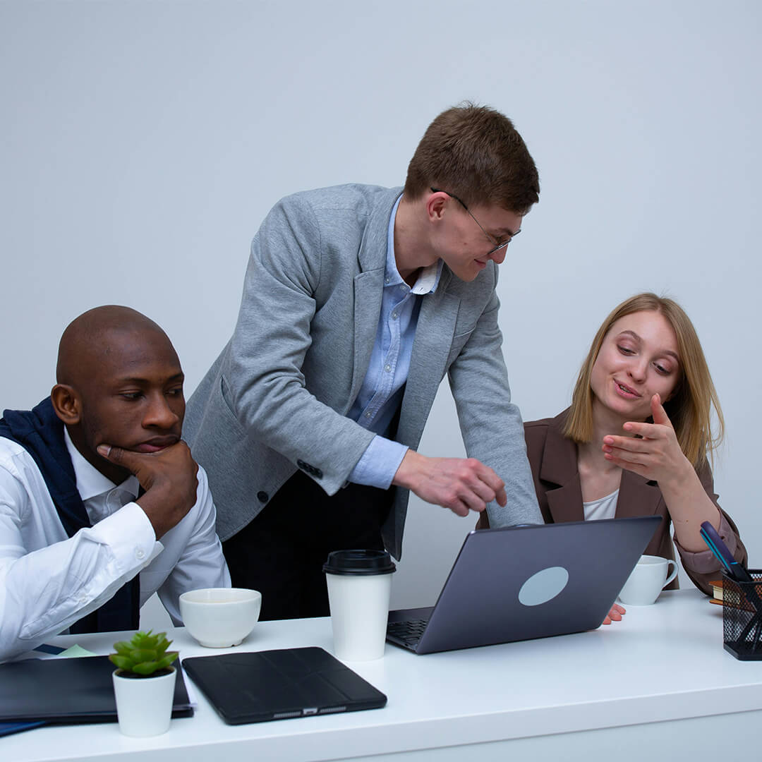 Man and two colleagues looking at laptops in office