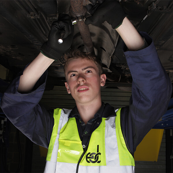 Young man in a high-vis jacket working on the underneath of a car.