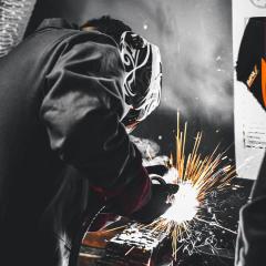 A person in welding masks welds metal with shooting sparks