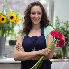 Woman in a blue apron clutches red flowers with sunflowers behind her