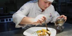 Hospitality student plating food and pouring sauce with a spoon