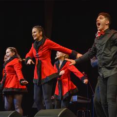 A group of performers in red and black outfits singing on stage