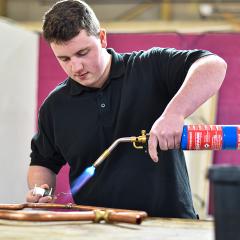 A young man using a blowtorch on copper piping