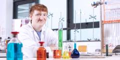 Boy in a lab coat with brightly coloured chemicals in front of him in glass jars