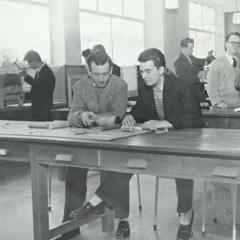 Black and white photo of two male student sat at a workbench