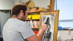 An art student drawing a picture, using charcoal, on an easel