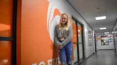EDC student Lucy Wood leaning against an orange wall with '6' graphic