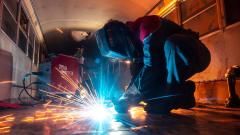 Someone wearing a protective mask and boiler suits welding metal