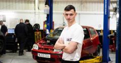 A photo of a young man wearing a white t-shirt with a red car in the background