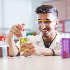 Student in a lab coat, smiling at the camera, holding a yellow chemical