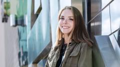 Smiling teenage girl standing in front of large silver East Durham College logo