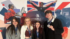 Four students standing in front of the World Skills UK Banner wearing their medals