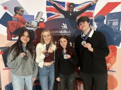 Media students holding bronze medals in front of World Skills signage