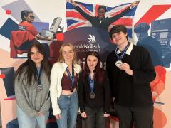 Four students holding their medals standing in front of a World Skills banner