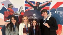 Four students holding their medals standing in front of a World Skills banner