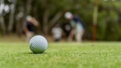 Golf ball on grass with two golfers in the background