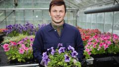 Smiling male student holding flowers in a greenhouse