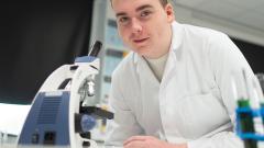 Scientist next to microscope smiling at camera