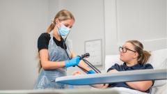 Student in mask testing the blood pressure of a smiling woman