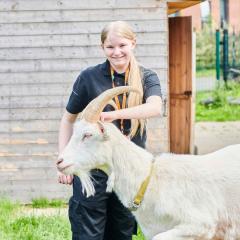 Female student smiling at camera whilst petting goat
